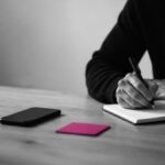 Persona che scrive concentrata con lo smartphone a faccia in giù sul tavolo