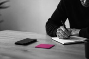 Persona che scrive concentrata con lo smartphone a faccia in giù sul tavolo Persona che scrive concentrata con lo smartphone a faccia in giù sul tavolo