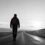 Uomo di spalle che cammina su una strada vuota all'alba: ricominciare e cambiare strada