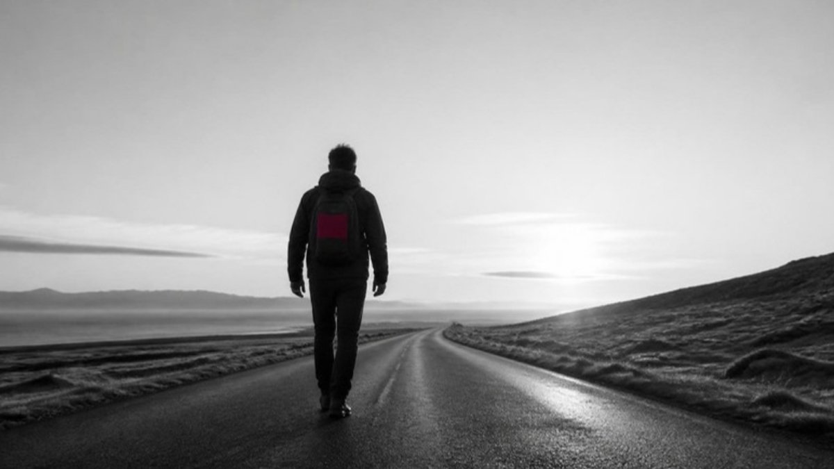 Uomo di spalle che cammina su una strada vuota all'alba: ricominciare e cambiare strada
